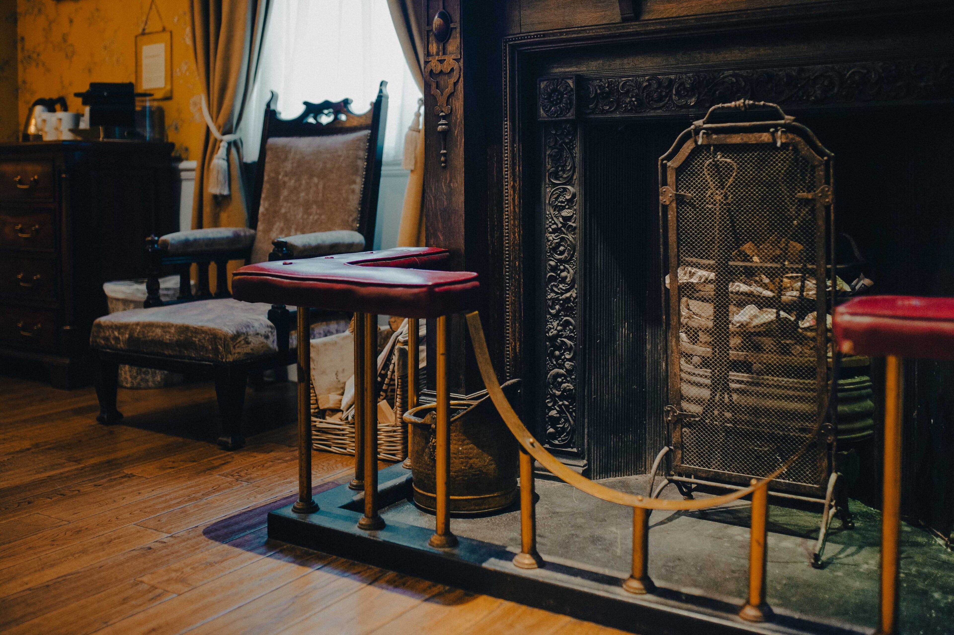 A room with a wooden floor, a fireplace, a red armchair, a small table, and a metal screen.