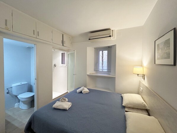 A bedroom with a bed, a window, a bathroom with a toilet, and a shower.
