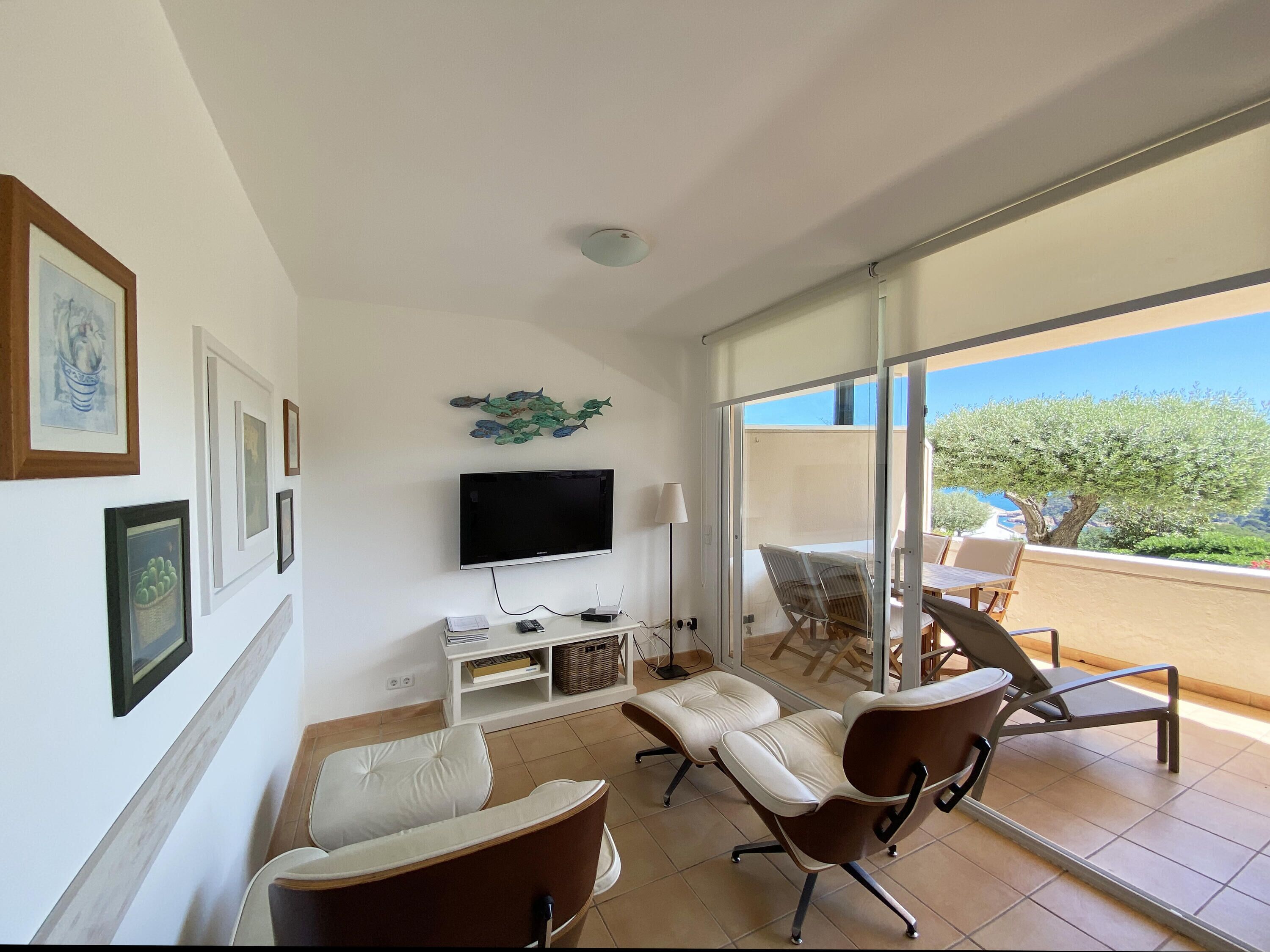 A modern living room with a flat-screen TV, comfortable seating, and a balcony with a view.