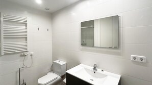Ein Badezimmer mit weißen Fliesen, einer Toilette, einem Waschbecken und einem Spiegel.