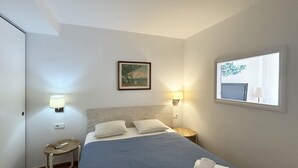 Ein Hotelzimmer mit Bett, zwei Nachttischlampen, einem kleinen Tisch, einem Gemälde an der Wand und einem Fenster mit Blick.