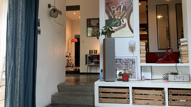 A modern living room with dark wooden flooring, a sofa, a coffee table, and a large poster. There is a staircase leading to another level, and a dining area with a red chair and a table. - House with garden in the city center (Marseille)