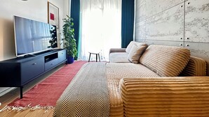 Una sala de estar moderna con una televisión de pantalla plana, un reloj grande, una planta en maceta, un sofá y una alfombra estampada.