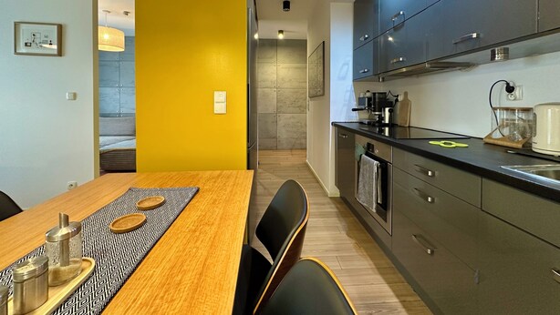 Una cocina moderna con armarios oscuros, una mesa de comedor de madera y una pared de acento amarilla.