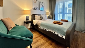 Una habitación de hotel moderna con una cama, un sillón verde y una ventana con cortinas.