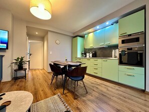 Una cocina moderna con armarios verdes, una mesa de comedor de madera y un horno empotrado.