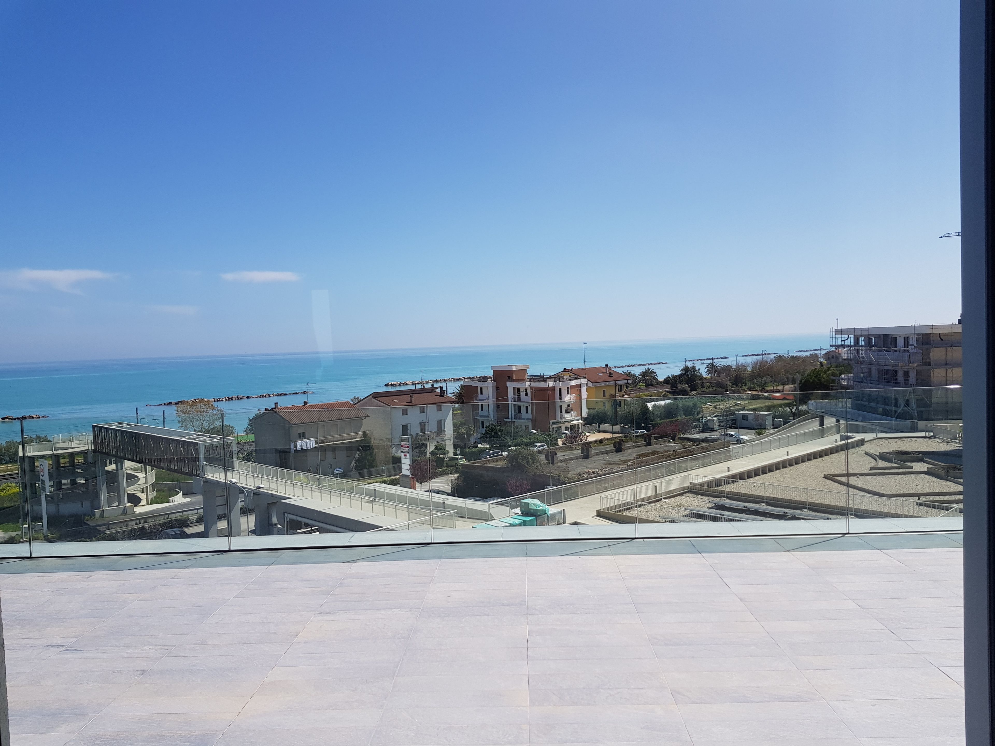 Vista di una zona costiera con edifici, cielo sereno e mare in lontananza.