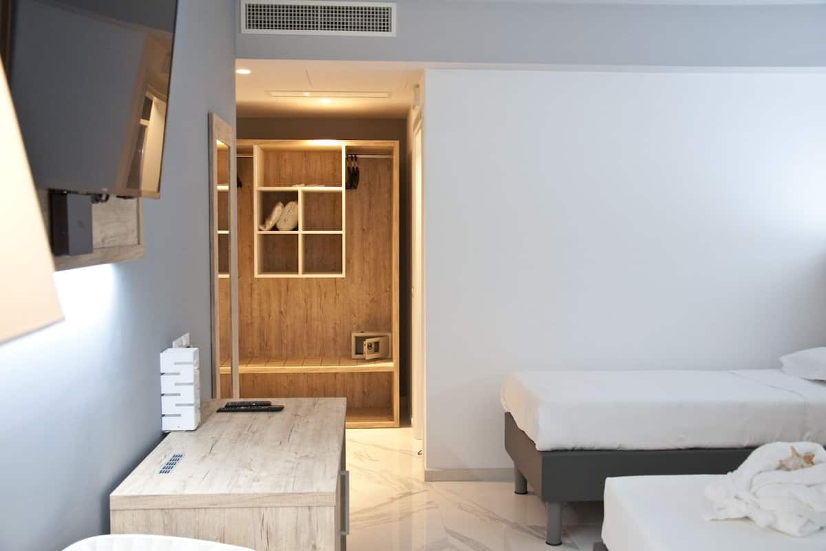 Een moderne hotelkamer met een houten garderobe, een klein tafeltje met een afstandsbediening, een bed en een witte badjas op de vloer.