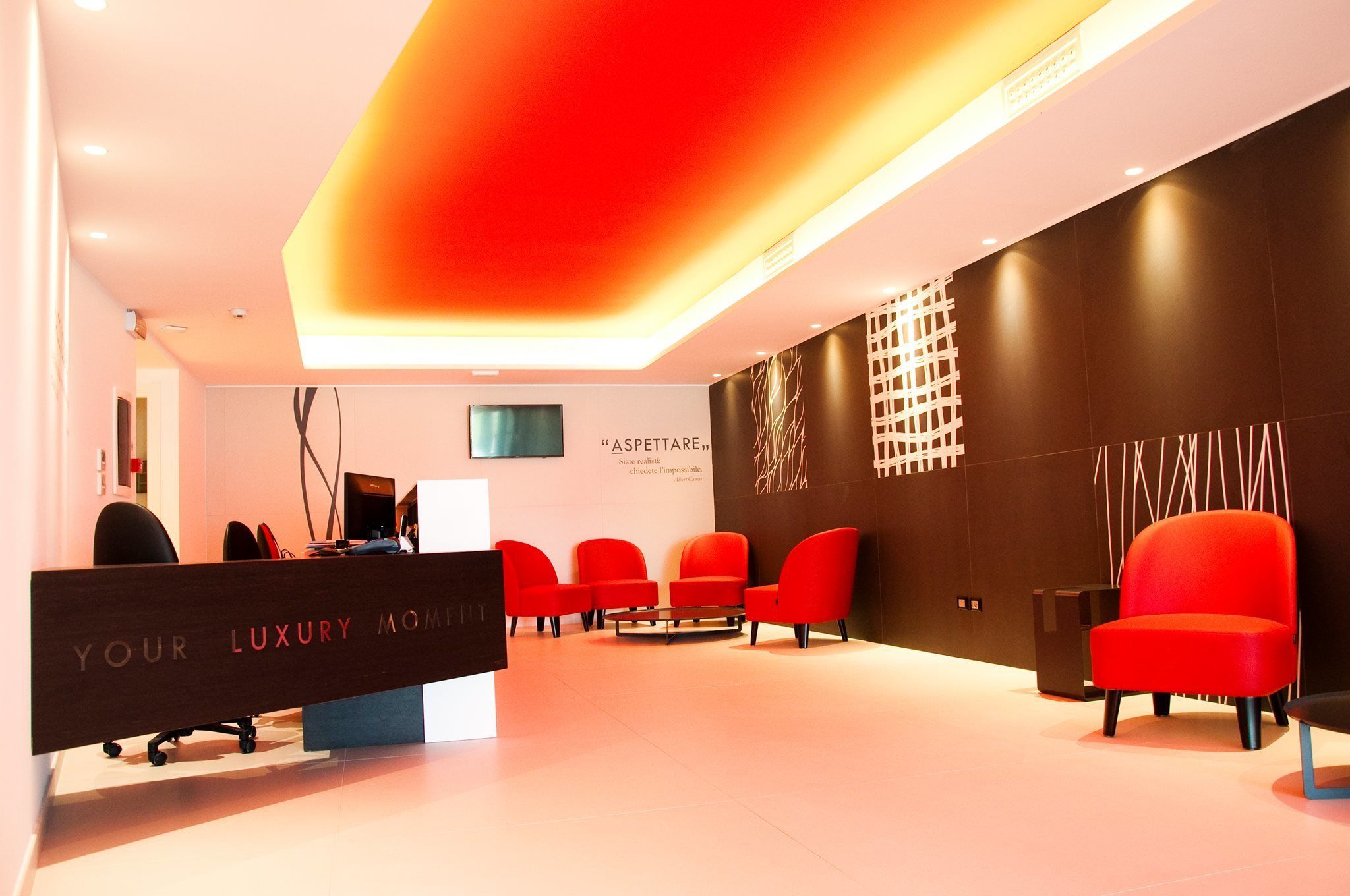 Una moderna área de recepción con una decoración en rojo y negro, un mostrador de recepción y varias sillas rojas.