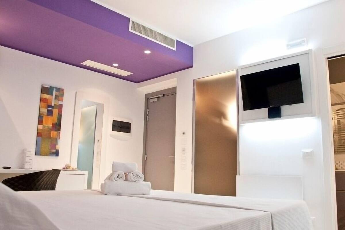 Een hotelkamer met een bed, een aan de muur bevestigde televisie, een handdoek op het bed, een deur en een raam.