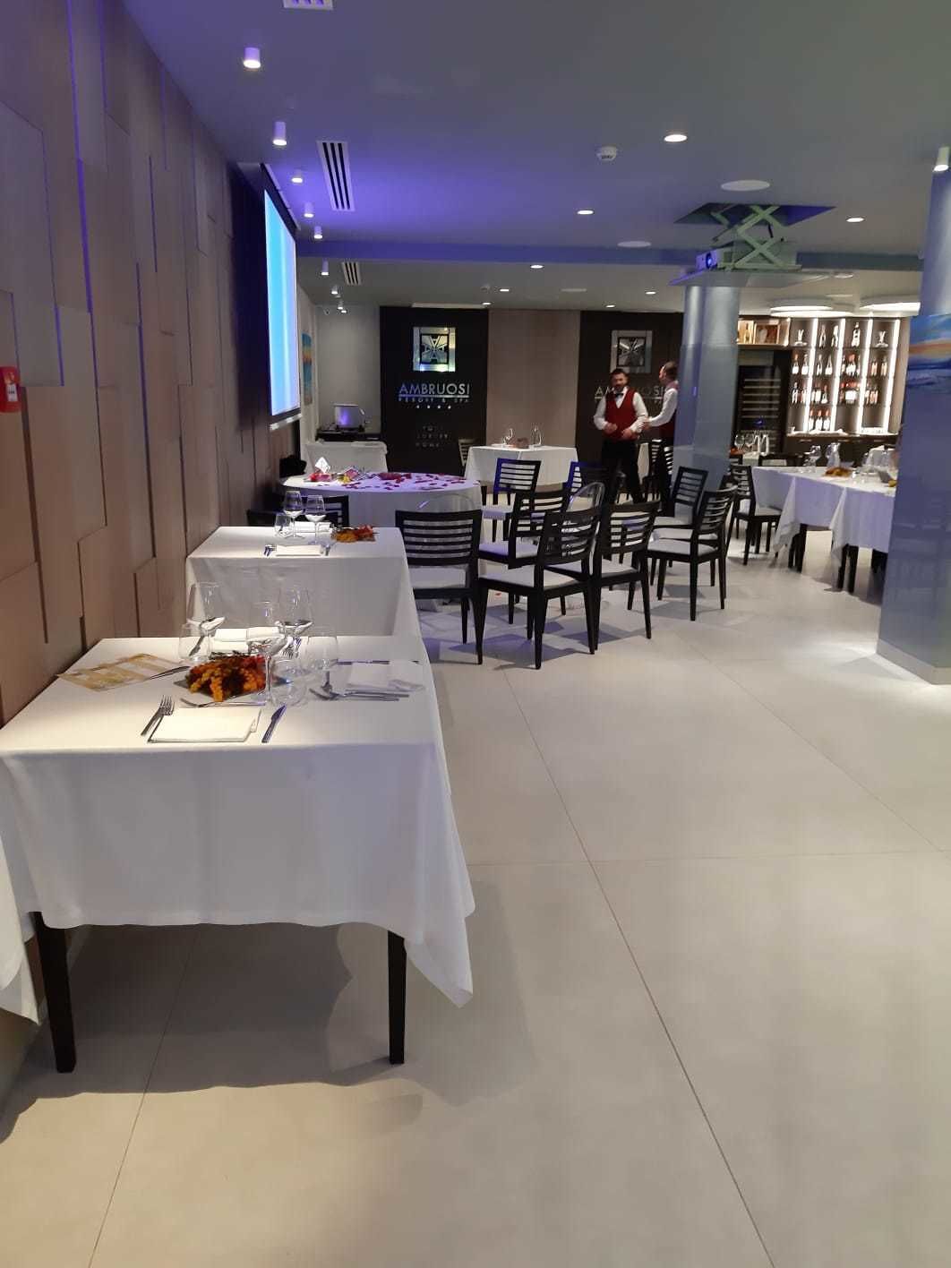 Um restaurante com várias mesas, cada uma com toalhas de mesa brancas e cadeiras.