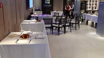 Um restaurante com várias mesas, cada uma com toalhas de mesa brancas e cadeiras.