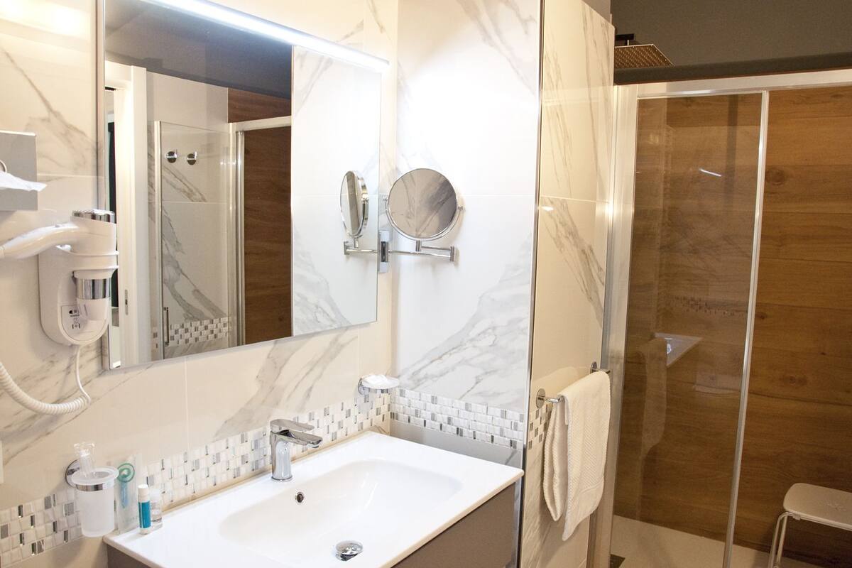 Een moderne badkamer met een marmeren wastafel, een douche met glazen wanden en een grote spiegel.