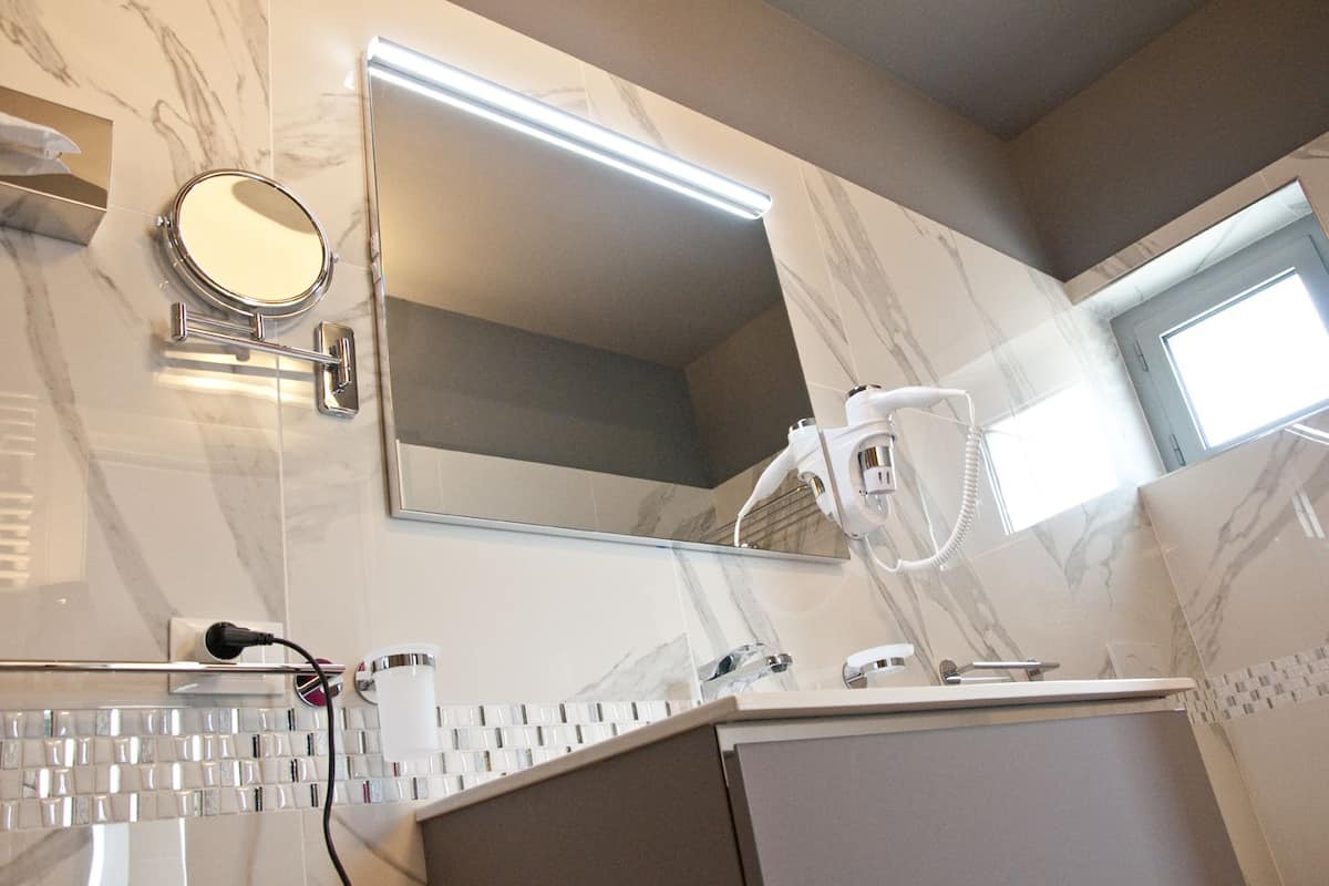 Een badkamer met een grote spiegel, een haardroger en een wastafelmeubel.