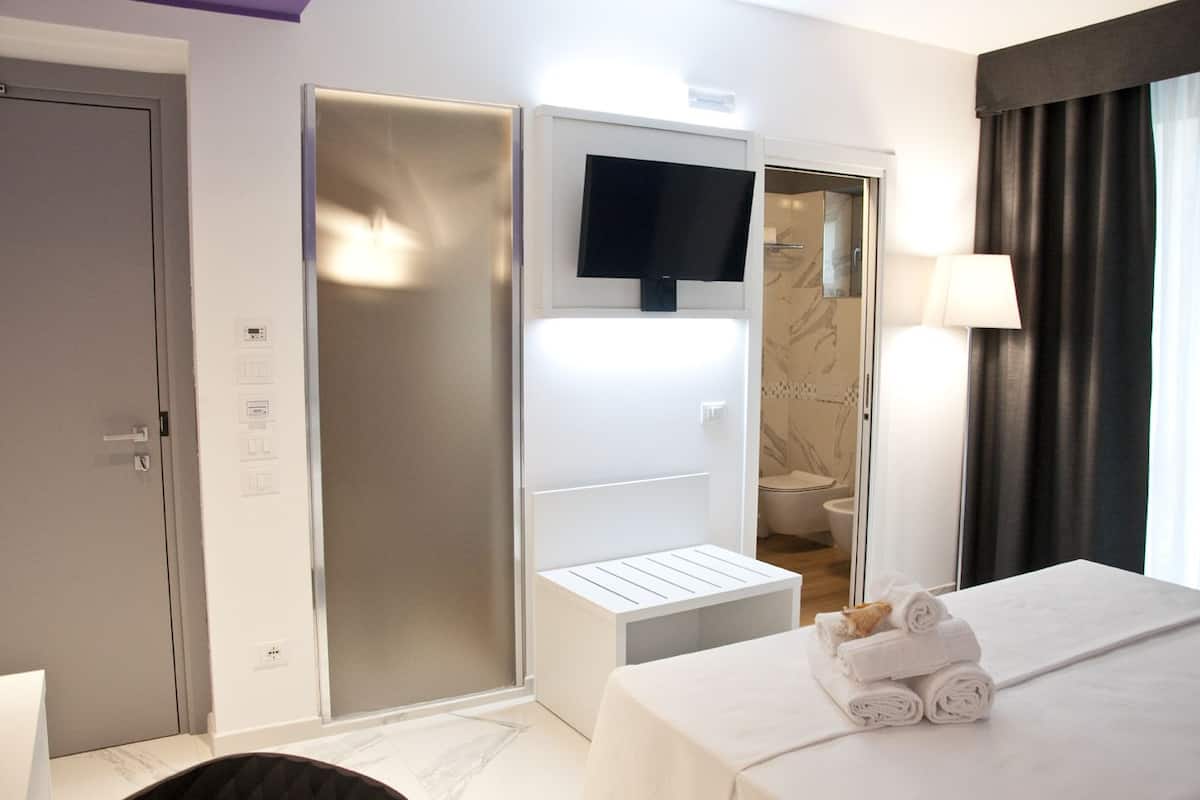 Hotelkamer met een bed, een aan de muur bevestigde televisie, een douche en een deur met bedieningspaneel.