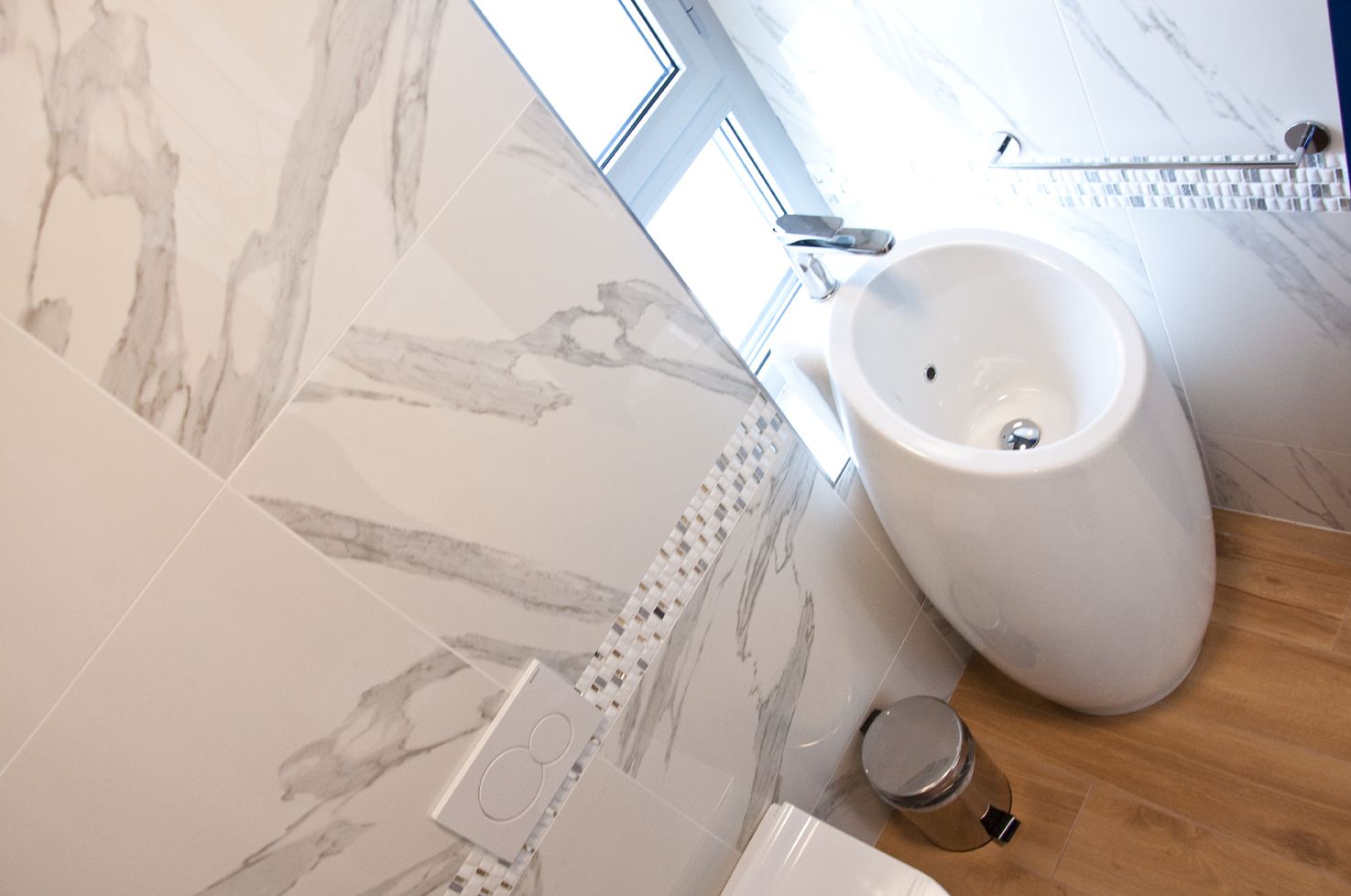 Une salle de bain moderne avec des carreaux de marbre, un bidet et un plancher en bois.