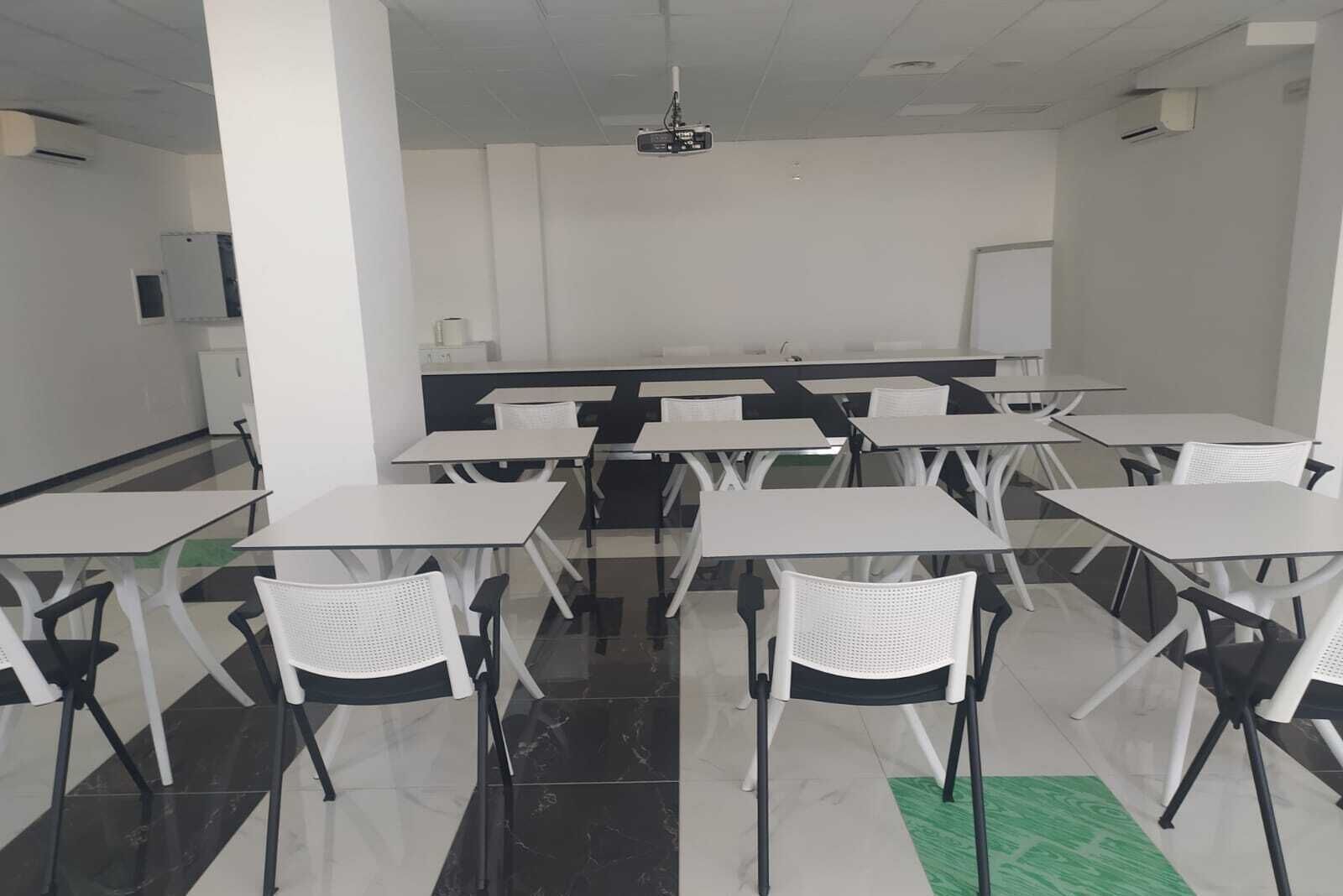 A classroom with white tables and chairs, a projector, and a whiteboard.