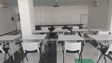 A classroom with white tables and chairs, a projector, and a whiteboard.