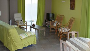 Een kamer met een bed, twee stoelen, een tafeltje, een televisie en een raam met gordijnen.