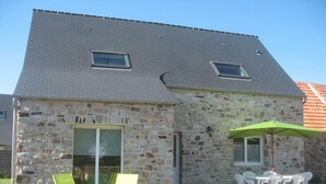 Een gebouw van steen met een schuin dak, twee ramen en een terras met tuinmeubilair.