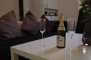 A bottle of champagne and two glasses on a white table in a living room with a sofa and cushions. - Langton House (Liverpool)