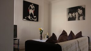 Un soggiorno con divano, televisore, un vaso con fiori e due quadri appesi al muro.