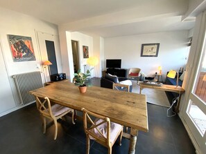 Uma sala de estar moderna com uma mesa de jantar de madeira, duas cadeiras, um sofá, uma TV e um abajur.