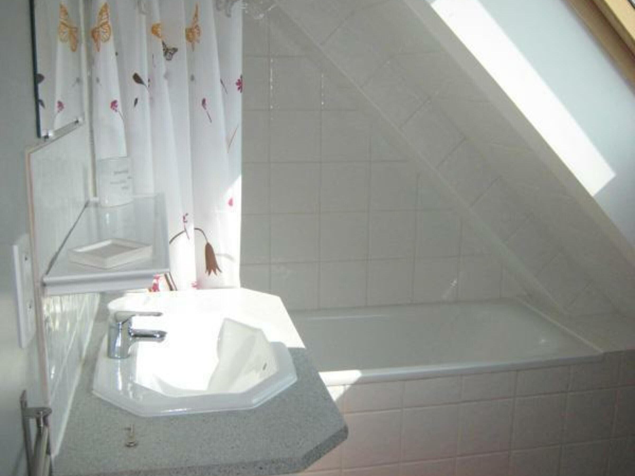 Un baño con lavamanos blanco, un espejo y zona de ducha.
