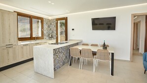Una cocina moderna con una isla grande, comedor con sillas y un televisor montado en la pared.
