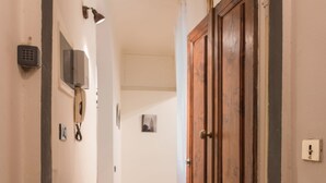 Een gang met een houten vloer, een deurmat en een deur met slot.