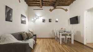 Een moderne woonkamer met een houten plafond, een grijze bank, een eettafel met stoelen en een flatscreen televisie die aan de muur is bevestigd.