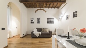 Een eetgedeelte met een witte tafel voor twee personen, een grijze bank en een houten plafond.
