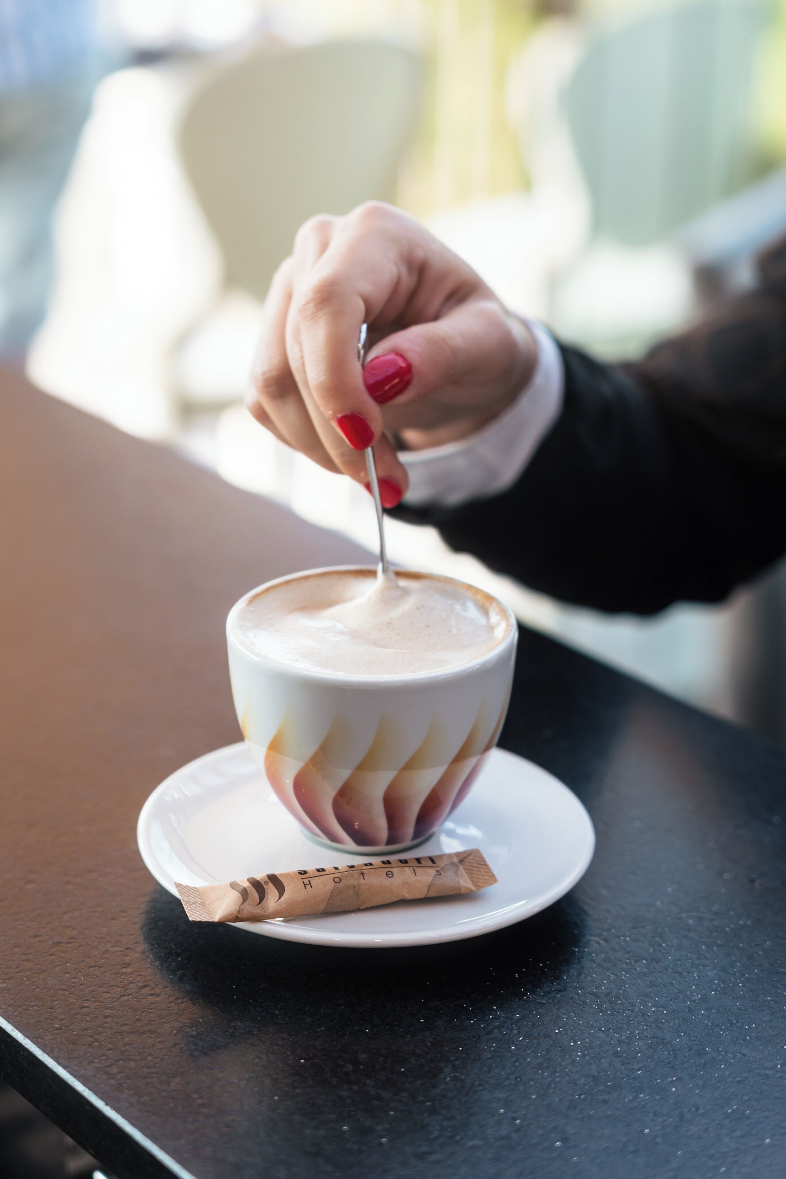 A hand stirring a cup of coffee on a saucer with a napkin beside it.