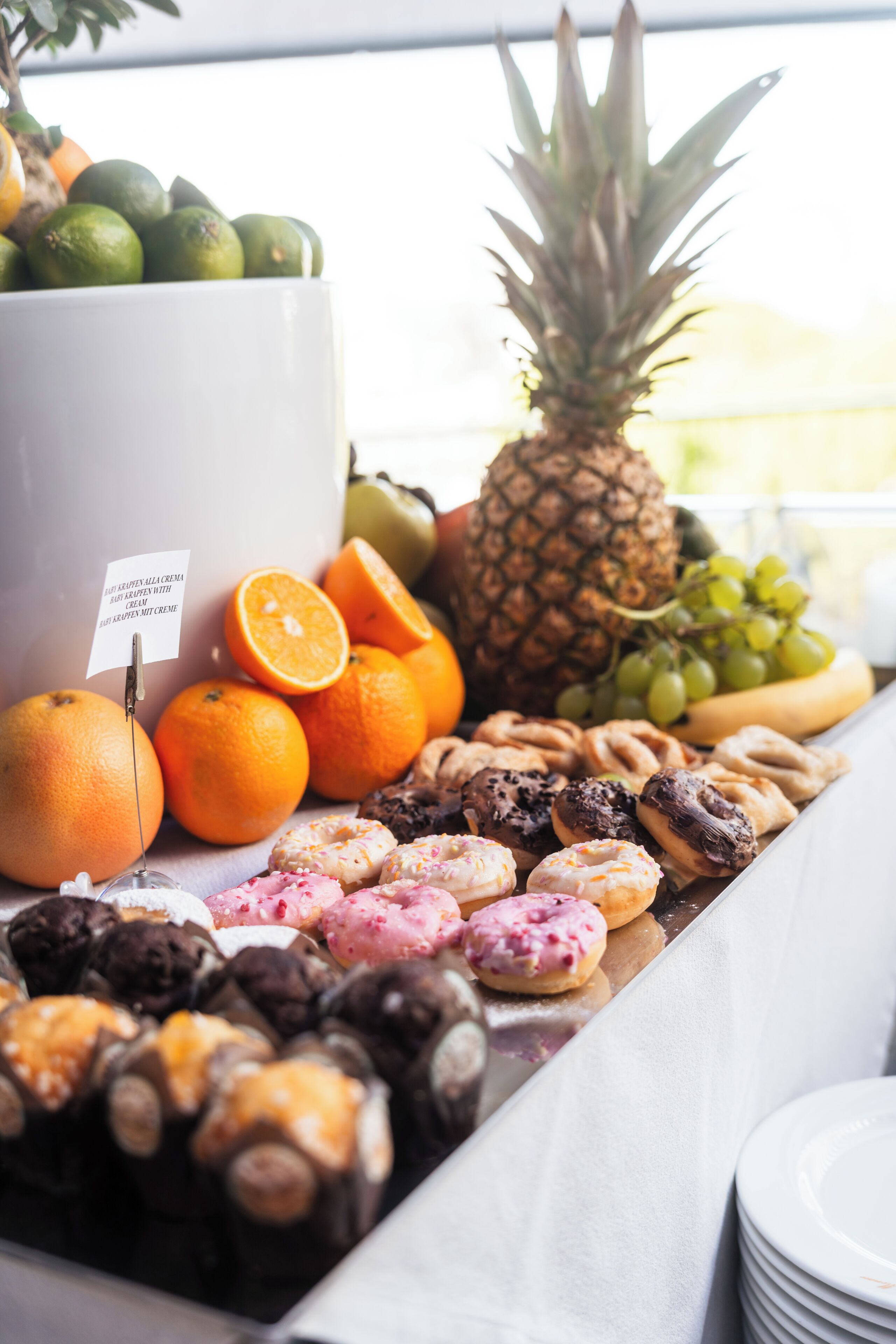 Une table de buffet proposant une variété de fruits, de pâtisseries, ainsi qu’un panneau indiquant la présence de crème et de sucre.