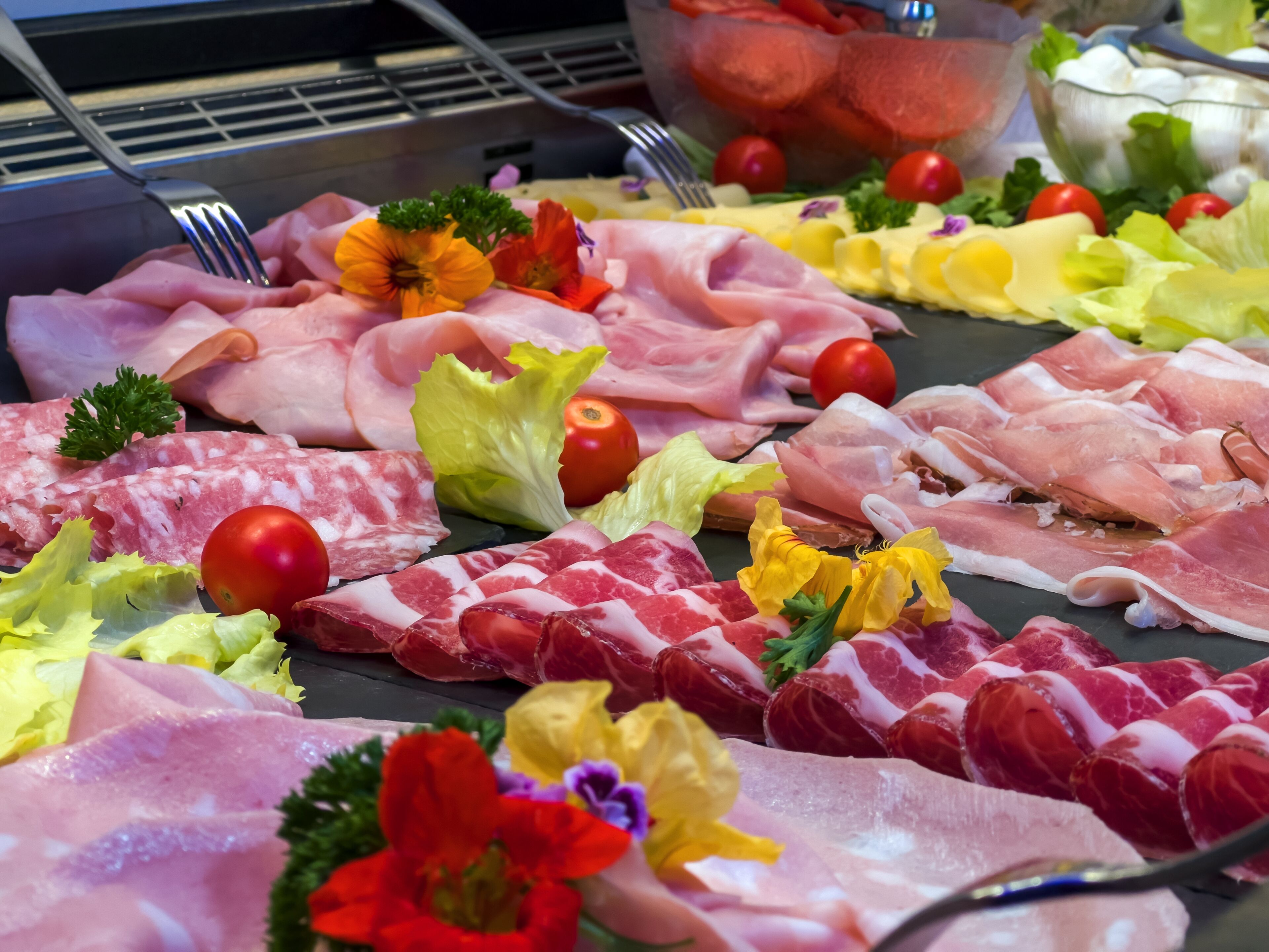 A variety of meats and vegetables on a table, including ham, salami, and lettuce.