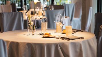 A dining table set with a bottle, glasses, a candle, and a flower.