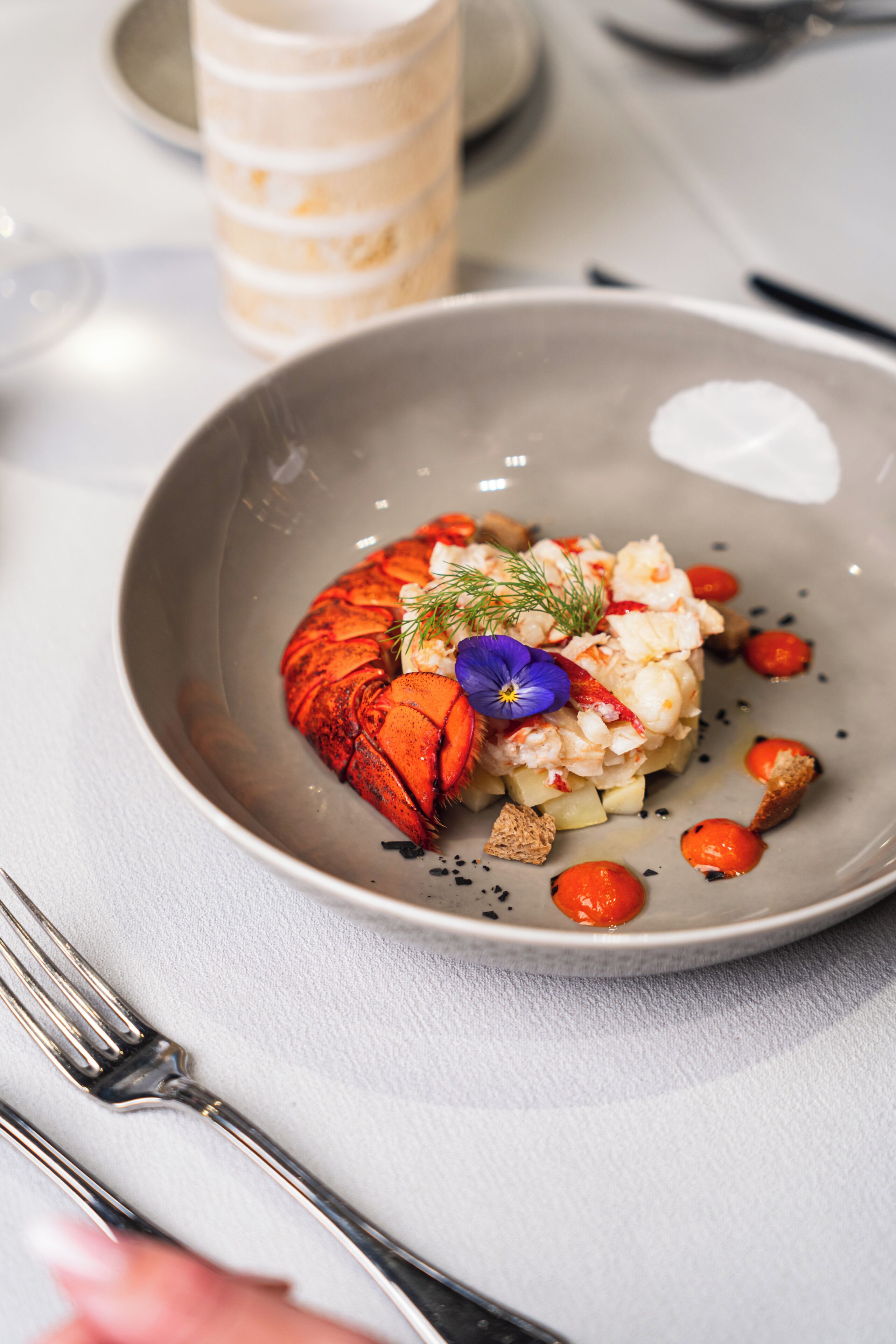 A plate with lobster, cream, and garnishes on a table.