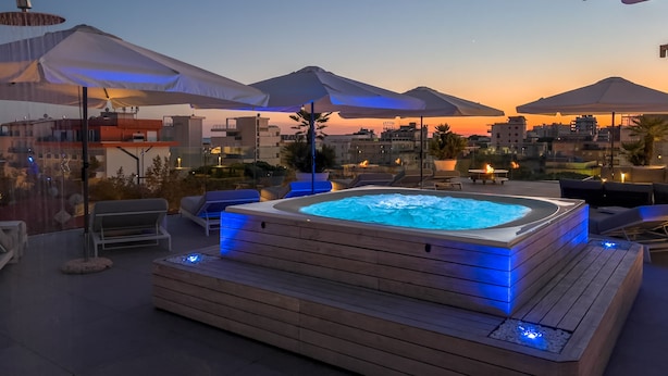 A rooftop terrace with a hot tub, outdoor seating, umbrellas, and city views at sunset. - Monaco Suites Hotel (Lignano Sabbiadoro)