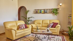 A living room with two yellow leather sofas, a coffee table, a patterned rug, a bookshelf, and a potted plant. - Villa Del Poggio (Castellammare del Golfo)