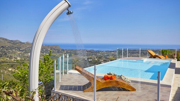 A modern outdoor pool with a curved water feature, surrounded by lounge chairs and a scenic view of the landscape. - Villa Del Poggio (Castellammare del Golfo)