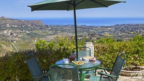 A table with chairs and an umbrella overlooking a scenic landscape with hills and the sea. - Villa Del Poggio (Castellammare del Golfo)