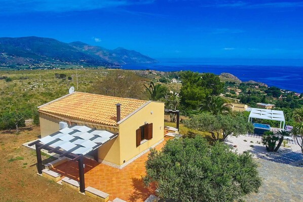 A yellow building with a tiled roof, a covered outdoor seating area, and a view of the sea and mountains.