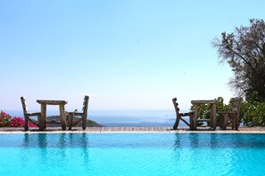 Une piscine entourée de chaises en bois, avec vue sur l’océan.