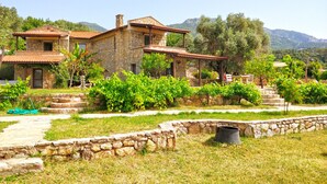 A stone house with a tiled roof, surrounded by a garden with grapevines and a stone wall. - Zephyros Hotel (Datça)