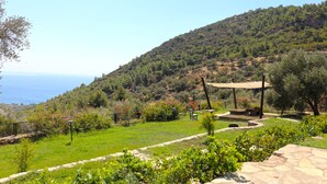 A lush garden with a pergola, seating area, and a view of the sea. - Zephyros Hotel (Datça)