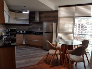 A modern kitchen with wooden cabinets, a stainless steel range, and a glass dining table with chairs. - HB Calacoto (La Paz)