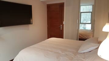 A bedroom with a bed, a TV mounted on the wall, a wardrobe, and a window.