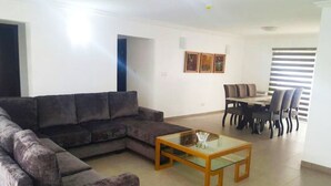A living room with a sectional sofa, a glass coffee table, and a dining area with a table and chairs. - Gemini Place Apartments (Lagos)