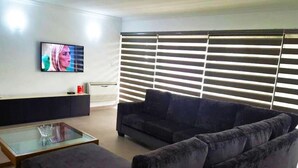 A living room with a dark-colored sofa, a glass coffee table, and a flat-screen TV mounted on the wall. - Gemini Place Apartments (Lagos)