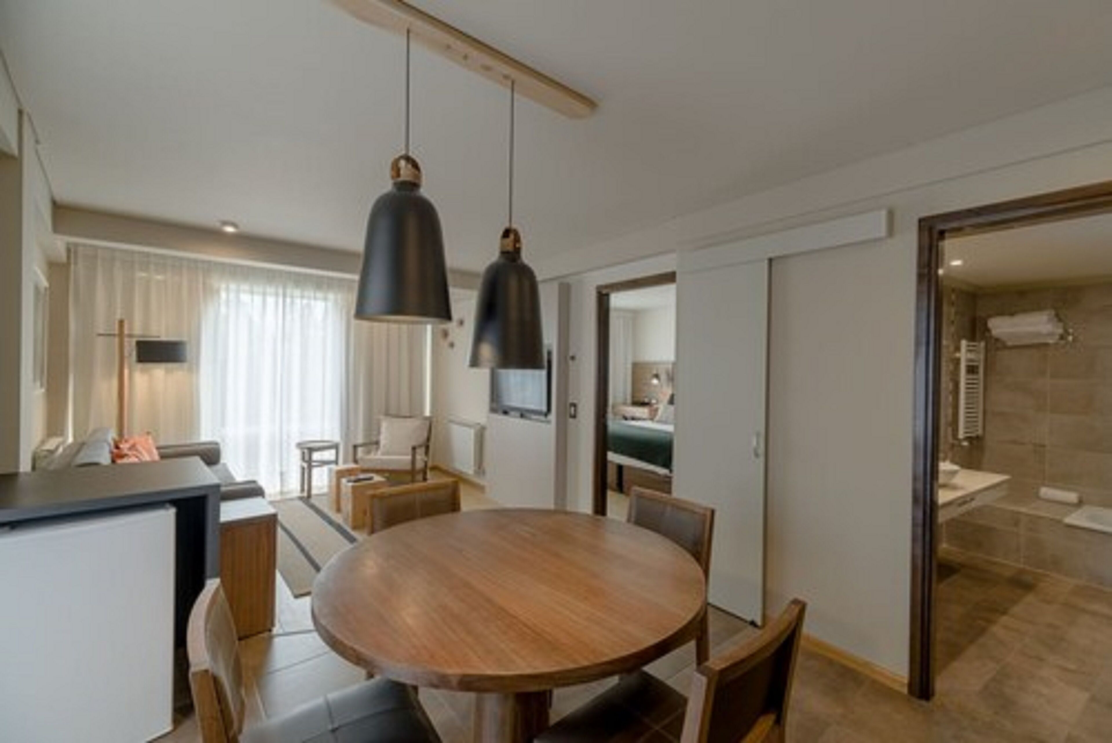 Een moderne keuken met een houten eettafel en stoelen, hangende lampen en uitzicht op de aangrenzende badkamer.